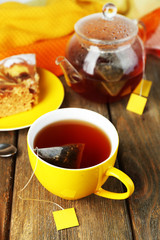 Cup with tea, teapot and tea bags on wooden table close-up