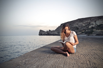 young beautiful girl who is reading a book on a pier