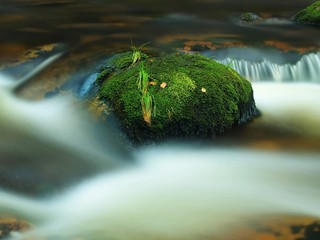 Dark big mossy stone rapid stream with blurred blue waves. 