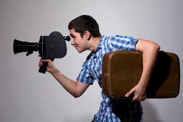 Young gay filmmaker with old movie camera and a suitcase in his