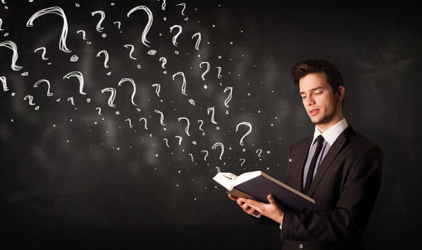 Young man reading a book with question marks coming out from it