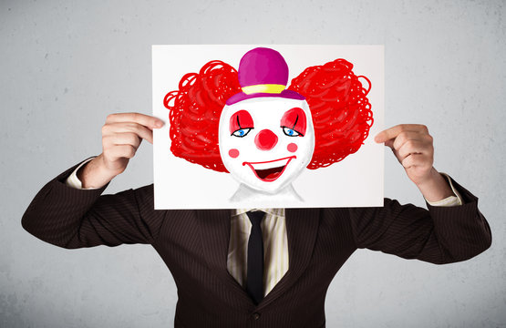 Businessman Holding A Cardboard With A Clown On It In Front Of H