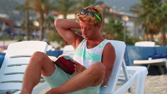 attractive young man reading a book on the beach
