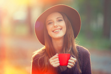 Beautiful redhead girl with cup in the park.