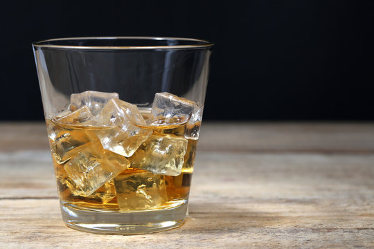 Whisky im Glas mit Eiswürfeln auf Holzbrett