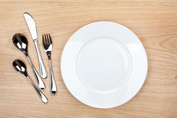Empty white plate with silverware on wooden table