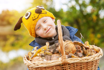 Little pretty boy in funny hat and big basket of mushrooms
