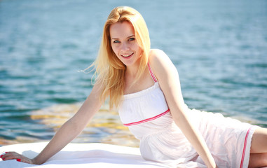 Pretty blond woman in a white dress on background of blue water