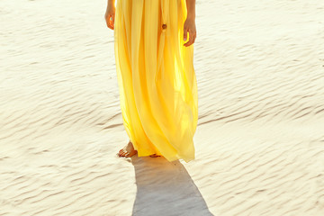 girl in a yellow dress walking barefoot on the white sand