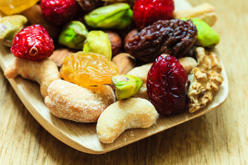 Varieties of dried fruits and nuts on wooden spoon.
