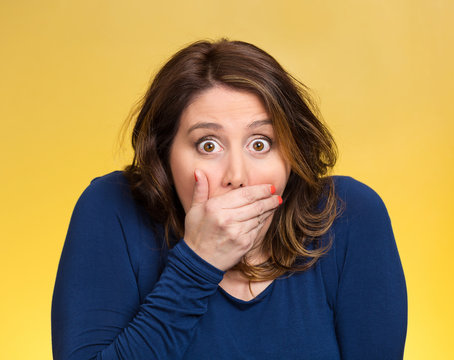 Shocked young woman covering her mouth yellow background 