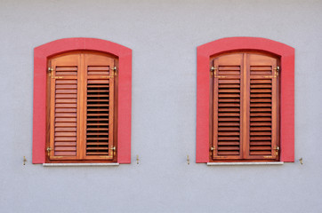 Two red windows with wooden jalousie on withe wall