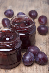 Jam from plums in two glass jars and plums on the table.