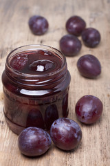 Plum jam in a glass jar and plums on the table.