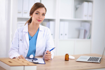 Beautiful young smiling female doctor sitting at the desk and w