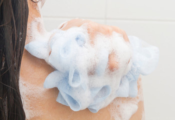 A Woman take a shower and clean her back with puff