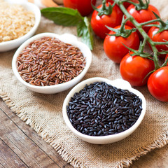 Variety of rice in bowls and tomatoes on wooden table