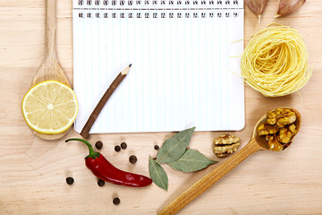 Notebook for recipes, vegetables and spices on wooden table.