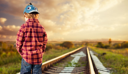 pencive boy in hat at railway sunset