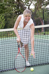 Female tennis reaching over the net to retrieve a ball
