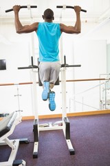 Rear view of muscular man doing pull ups at gym