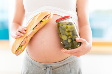 Pregnant woman with sandwich and jar of pickles