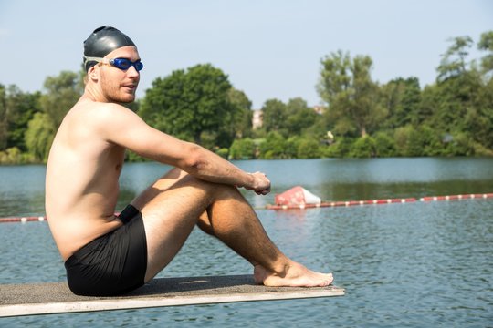 Man sitting on diving board in the sun at lake