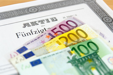 Aktie mit aufgefächerten Geldscheinen und Tiefenschärfe