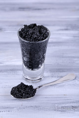 Fototapeta na wymiar Glass and spoon of black caviar on grey wooden background