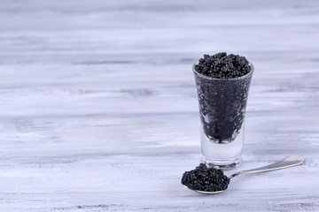 Fototapeta na wymiar Glass and spoon of black caviar on grey wooden background