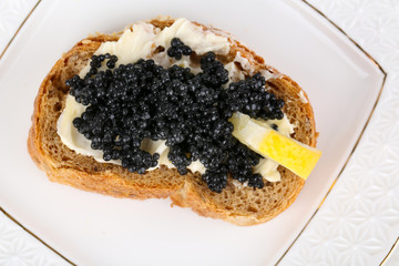Slice of bread with butter, black caviar and lemon