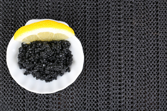Black caviar with lemon on plate on dark fabric background