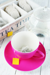 Cup and teapot with tea bags on wooden table close-up