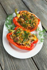 Stuffed red peppers with greens on plate on wooden table