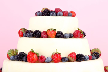 Beautiful wedding cake with berries on pink background