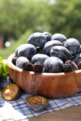 Ripe sweet plums in wooden bowl, on  nature background