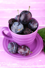 Ripe sweet plums in big cup, on pink wooden table