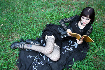 Sexy Witch reading spell book on the grass