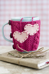 Blue cup in pink sweater with felt hearts standing on notebook