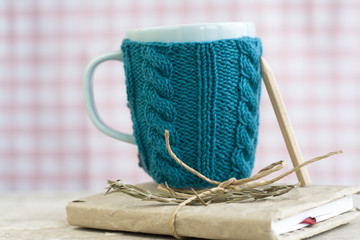 Blue cup in a blue sweater standing on an old notebook