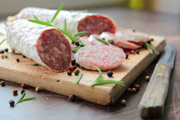 Sliced salami sausage on a wooden cutting board with herbs