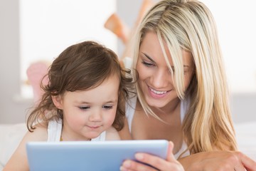 Mother and daughter using digital tablet on bed