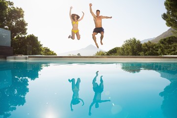 Cheerful couple jumping into swimming pool - Powered by Adobe
