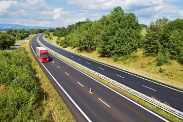 Obraz premium The rural landscape with a highway lined with trees, red truck
