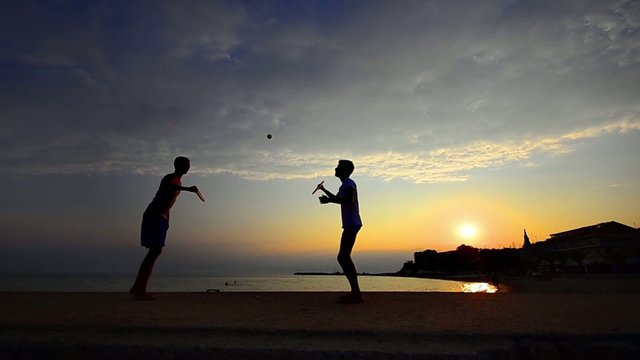 Boys playing ping pong on the beach at sunset
