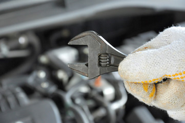 Hand wearing glove holding wrench in front of car engine 