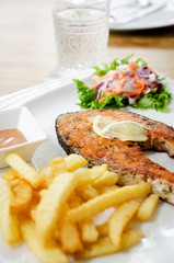 grilled salmon steak served with salad, chips,