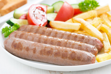 grilled sausages with French fries and vegetables, close-up