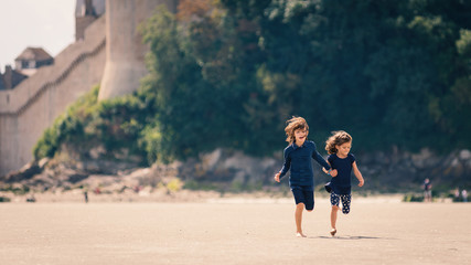 Young sisters running on the beach in front of Mont Saint Michel - obrazy, fototapety, plakaty