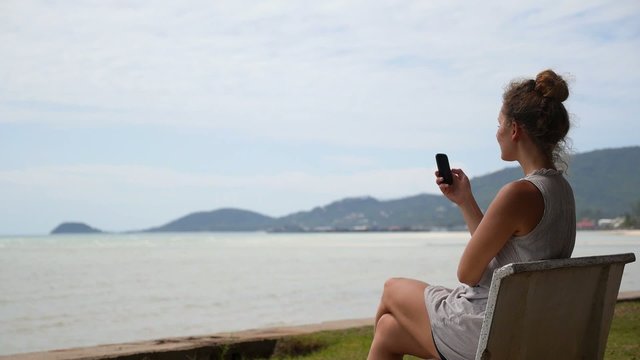 Pretty Teenager Girl Using Smart Phone Sitting at the Sea.